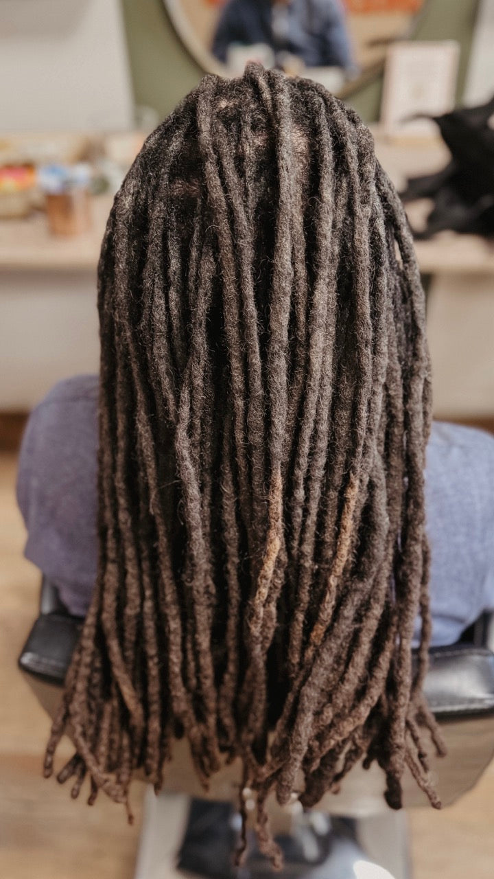 Person with long, real dreadlocks sitting in a salon chair in Dreadshop Salon. Long dark dreadlocks