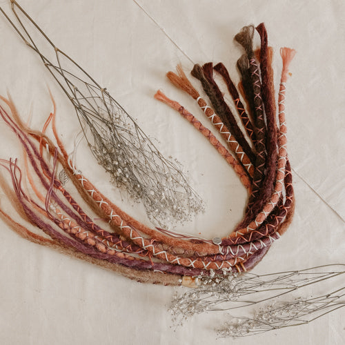 A set of handmade bohemian decorated dreadlock extensions Locks of Love in different colors, pink lavender purple and dark brown caramel tones. View from afar 