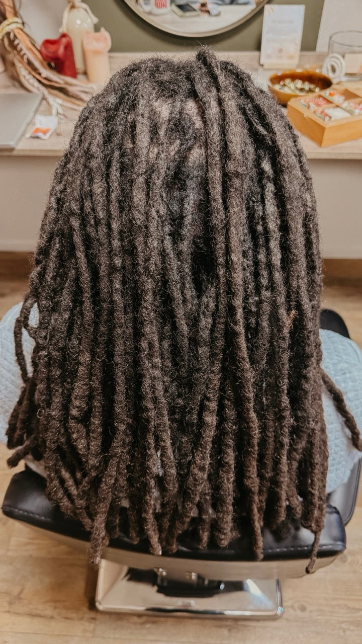 Person with long, real dreadlocks sitting in a salon chair in Dreadshop Salon